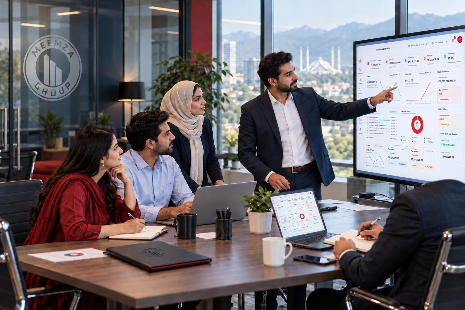 Meemza team reviewing the official Manuta Business Overview dashboard on a wall monitor and laptop
